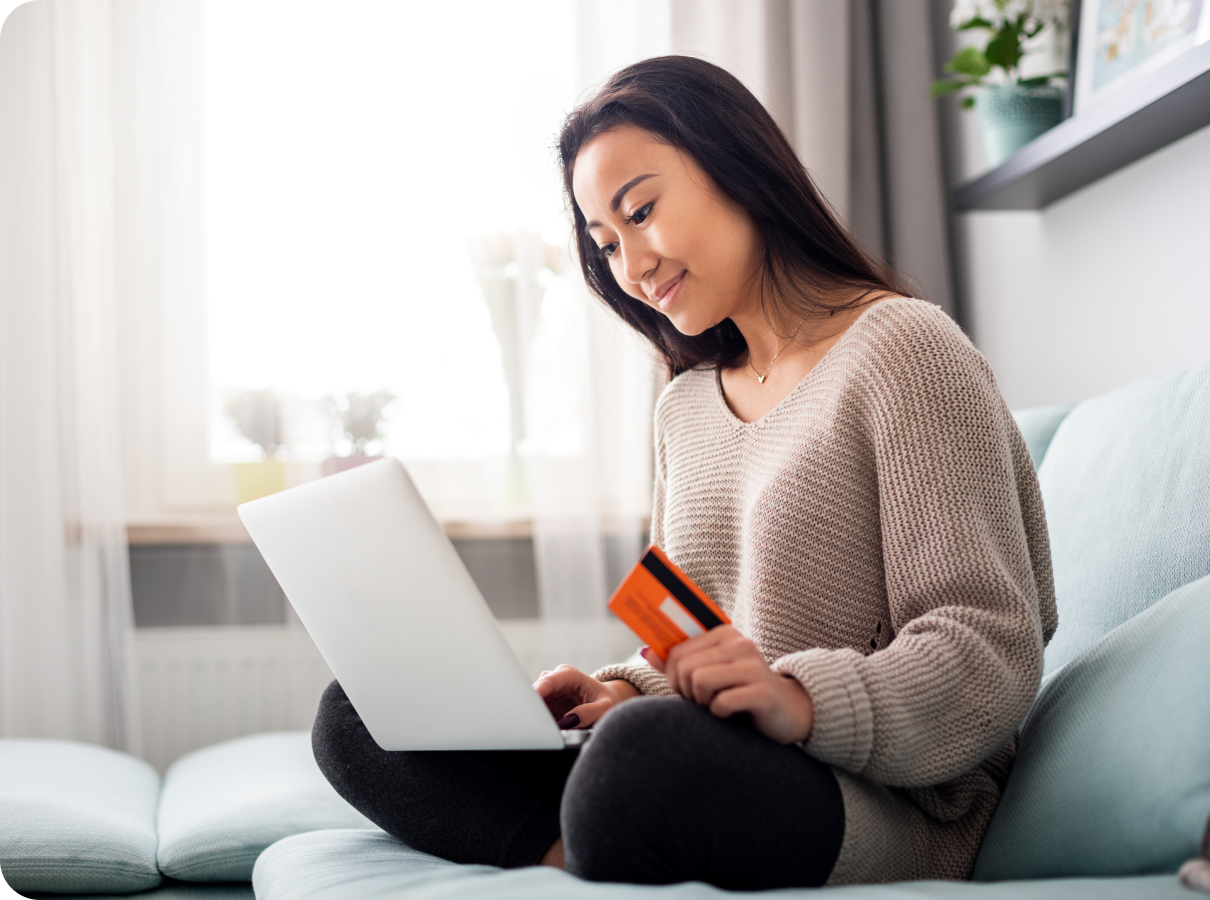 a woman sitting on a couch holding a credit card and a laptop.